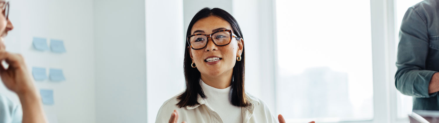 Eine Frau mit Brille erklärt im Büro einem Kollegen etwas 